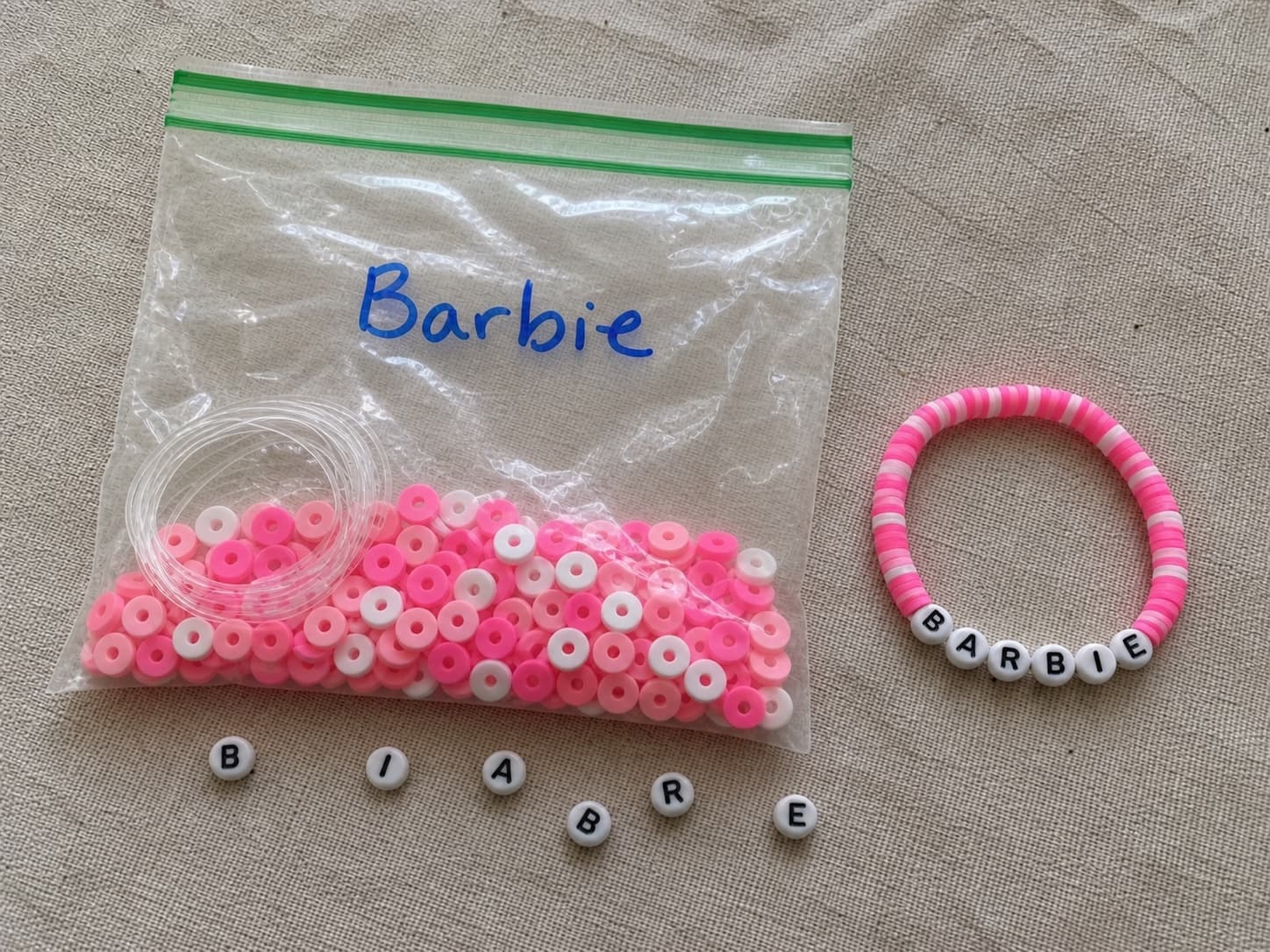 Handmade BARBIE bracelet beside its clear DIY bead kit and loose letter beads