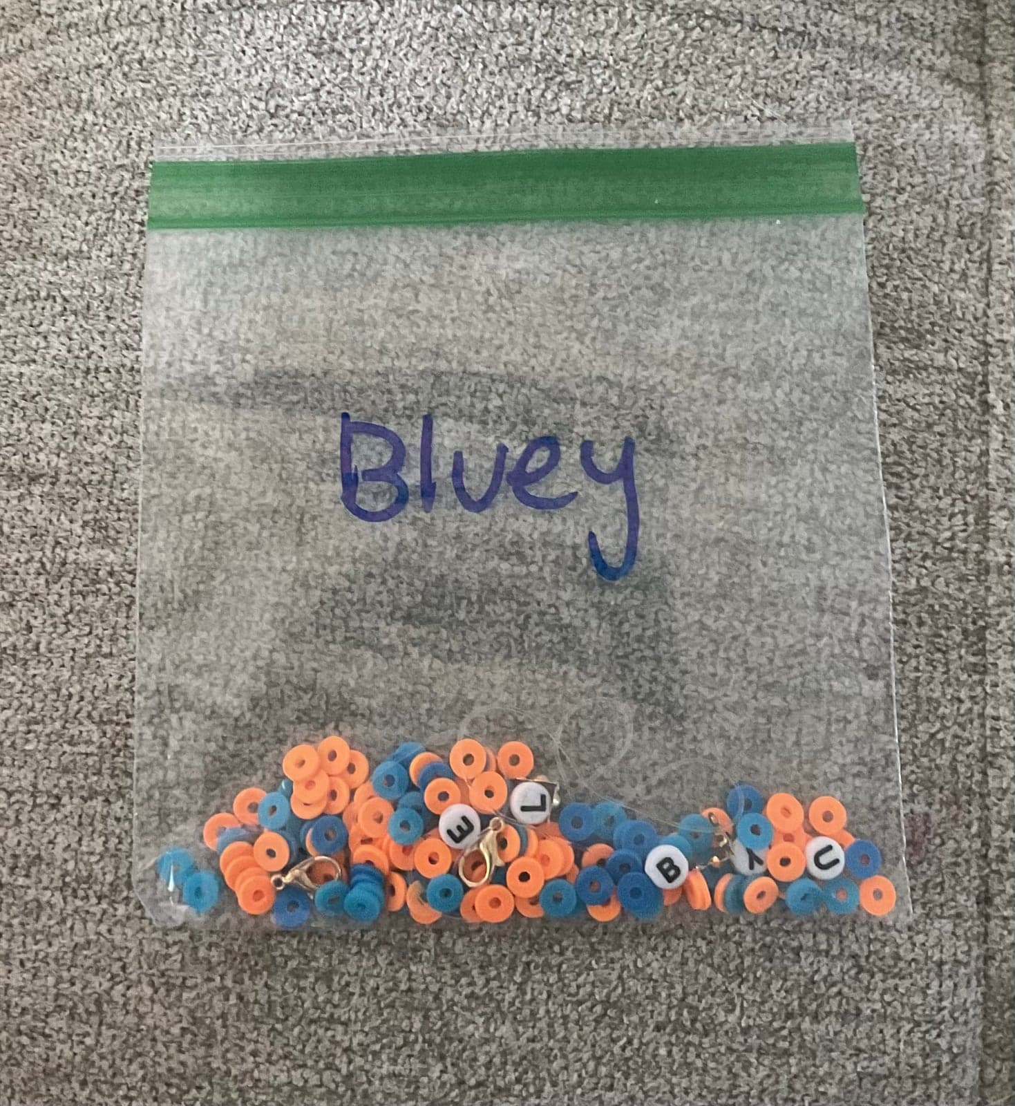 Blue and orange beads arranged beside a handmade letter bracelet