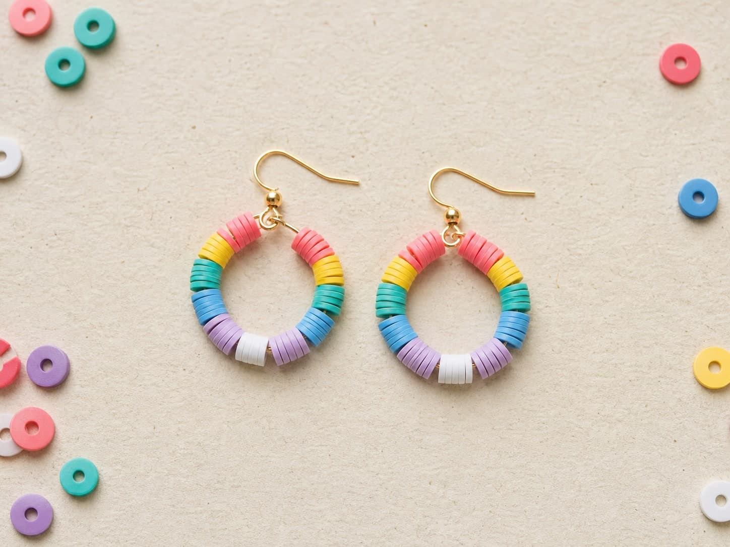 Rainbow clay-bead hoop earrings on a cream craft surface
