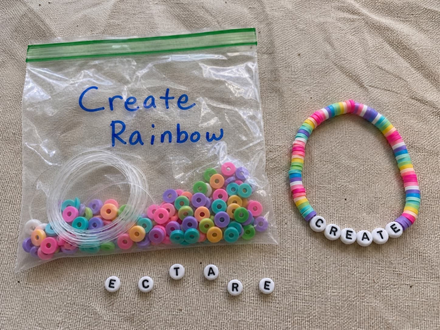 Handmade CREATE bracelet beside its clear DIY bead kit and loose letter beads