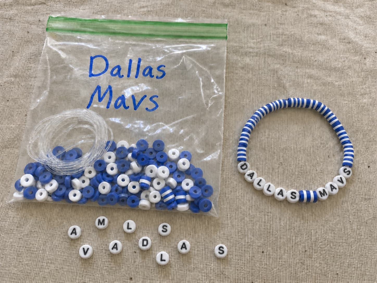 Handmade blue and white DALLAS MAVS bracelet beside its clear DIY bead kit and loose letter beads