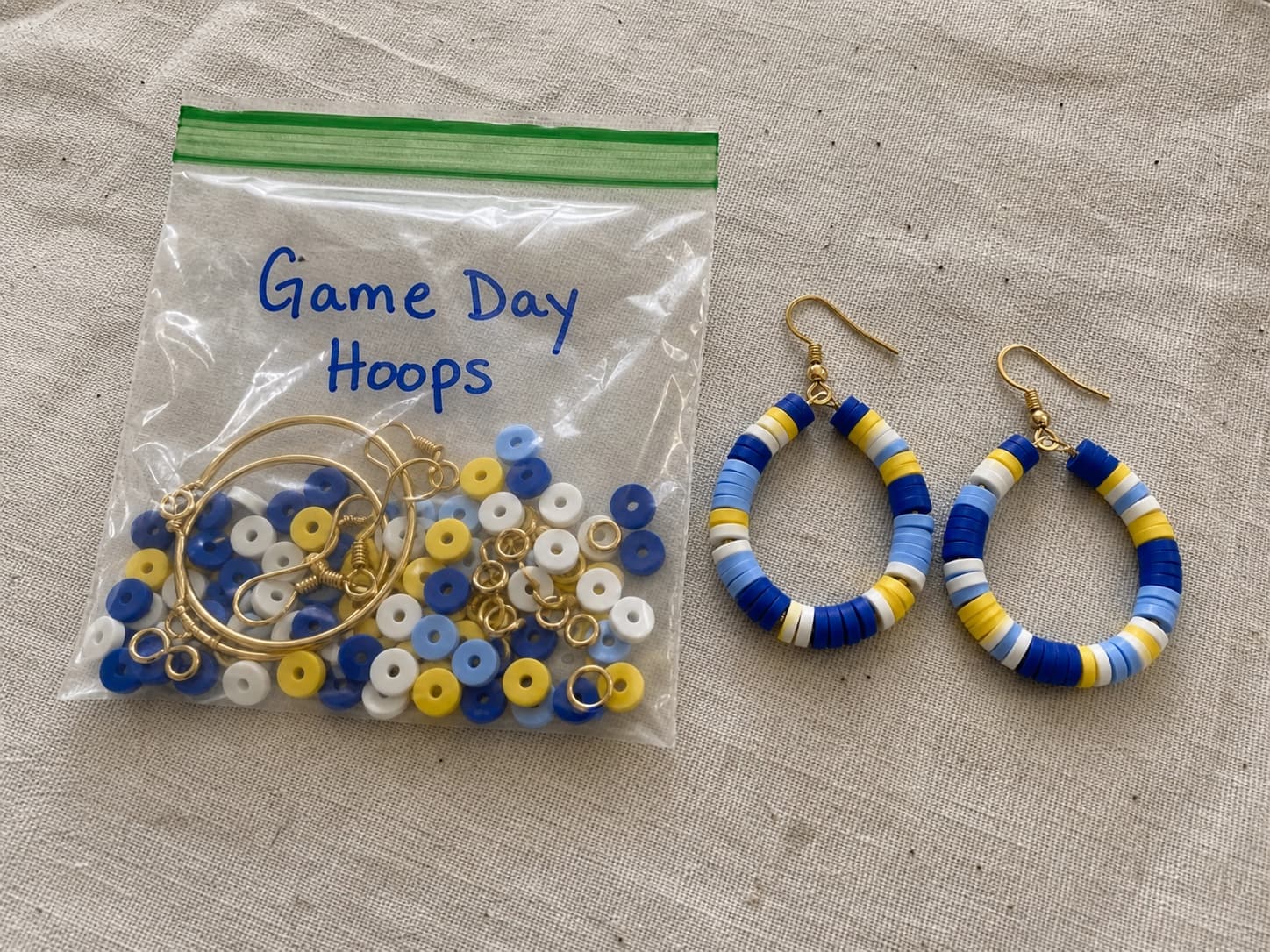 Handmade blue, yellow, and white Game Day hoop earrings beside their clear DIY kit