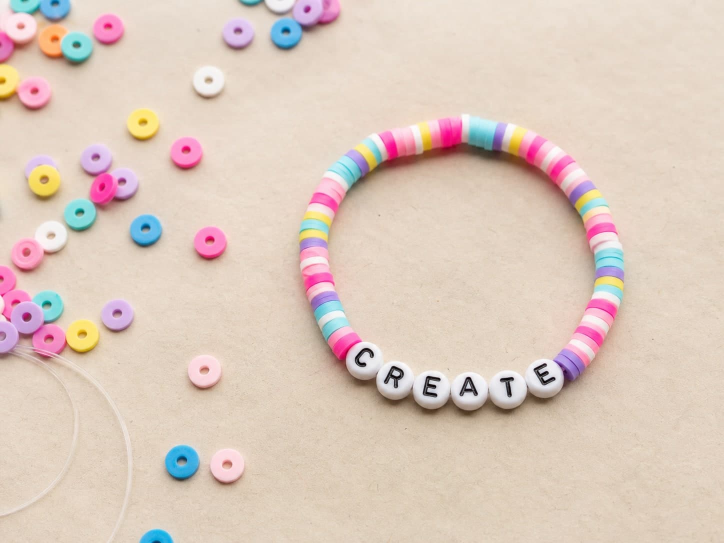 Rainbow clay-bead bracelet spelling CREATE on a craft table
