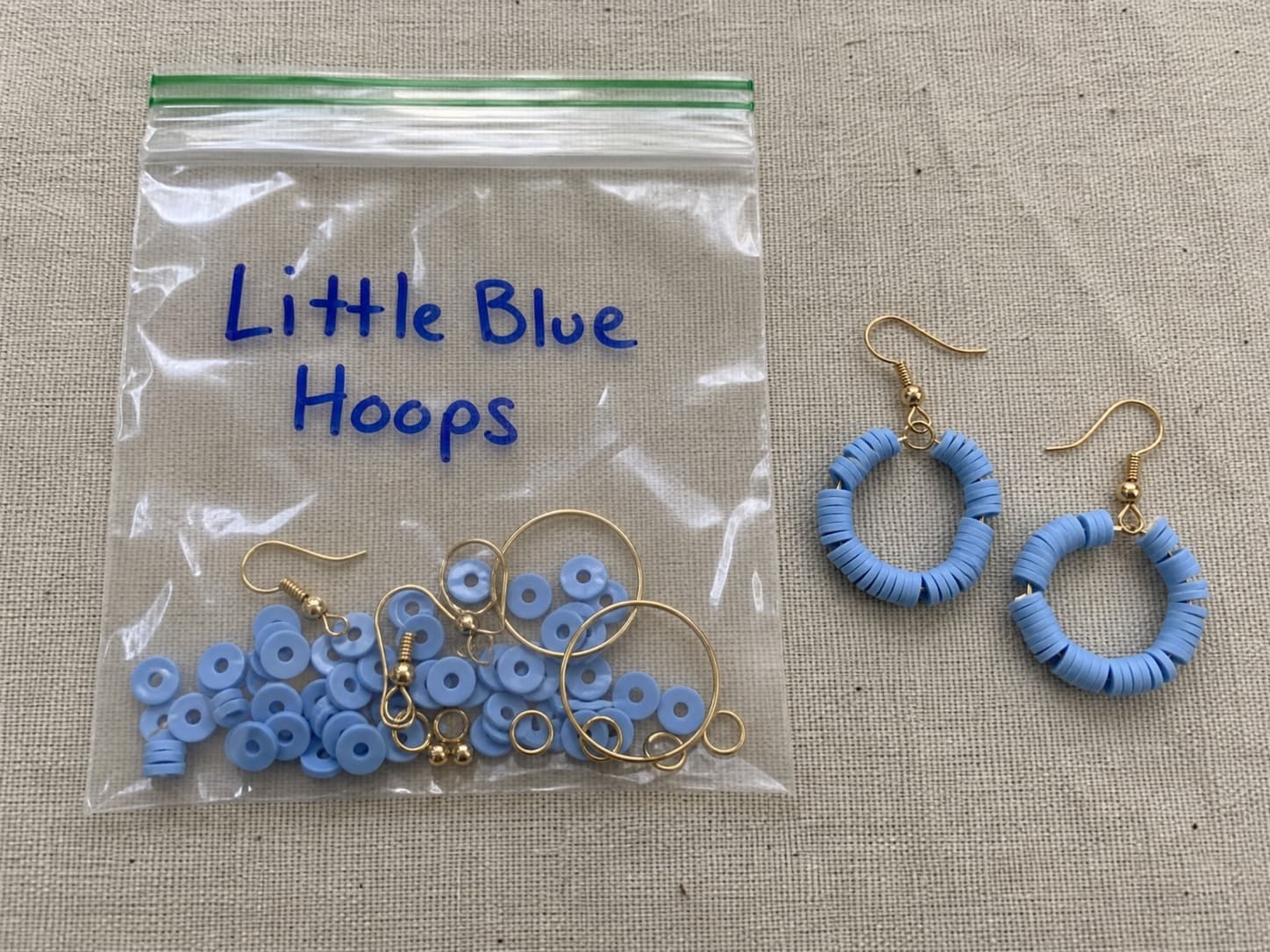 Handmade little blue hoop earrings beside their clear DIY bead and hardware kit