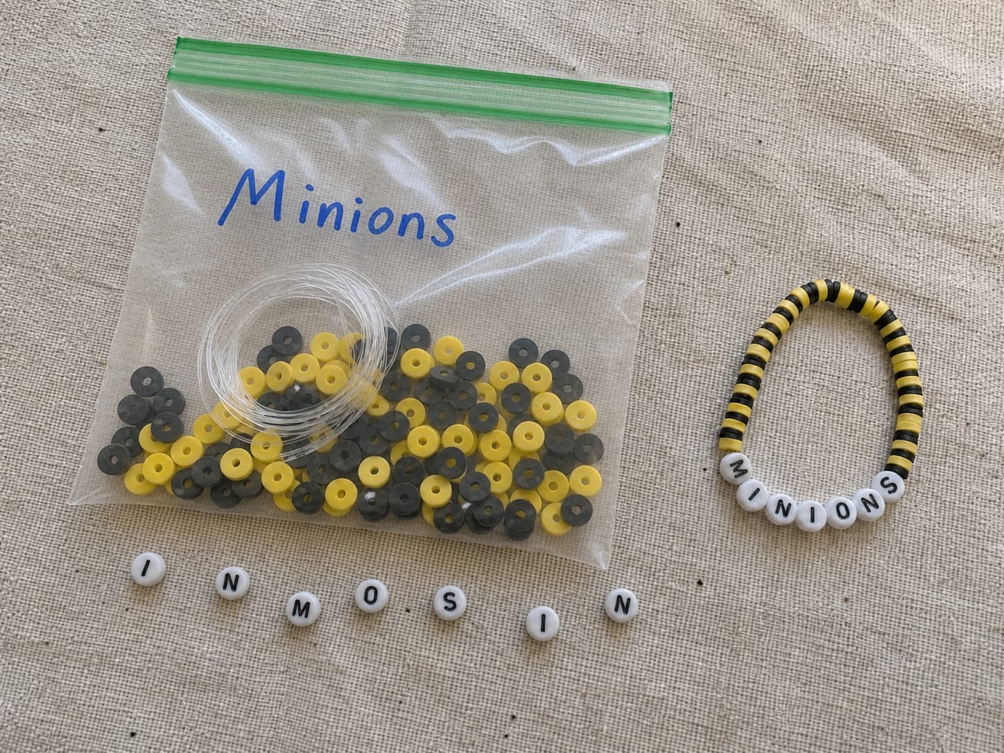 Handmade yellow and black MINIONS bracelet beside its clear DIY bead kit and loose letter beads