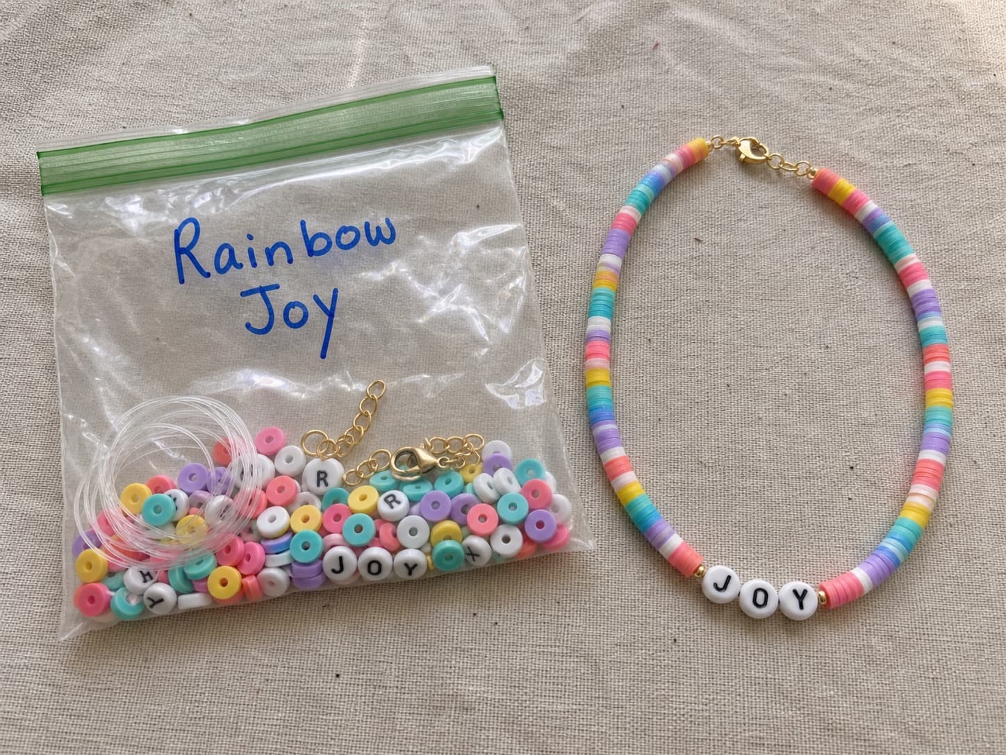 Handmade rainbow JOY necklace beside its clear DIY bead kit