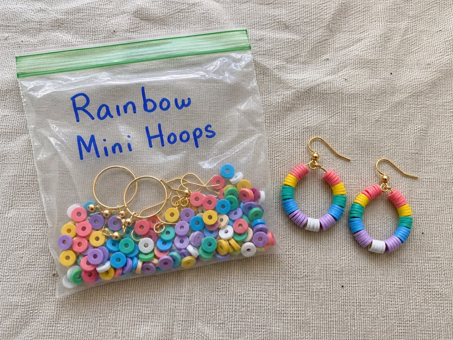 Handmade rainbow mini hoop earrings beside their clear DIY kit