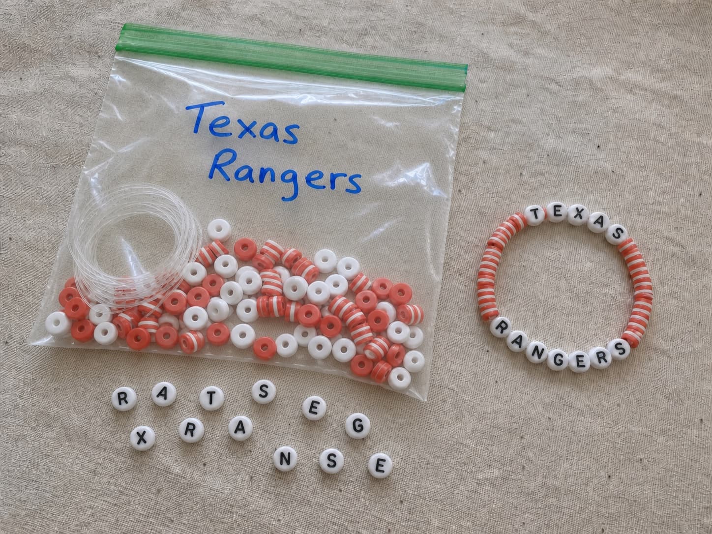 Handmade red and white TEXAS RANGERS bracelet beside its clear DIY bead kit and loose letter beads
