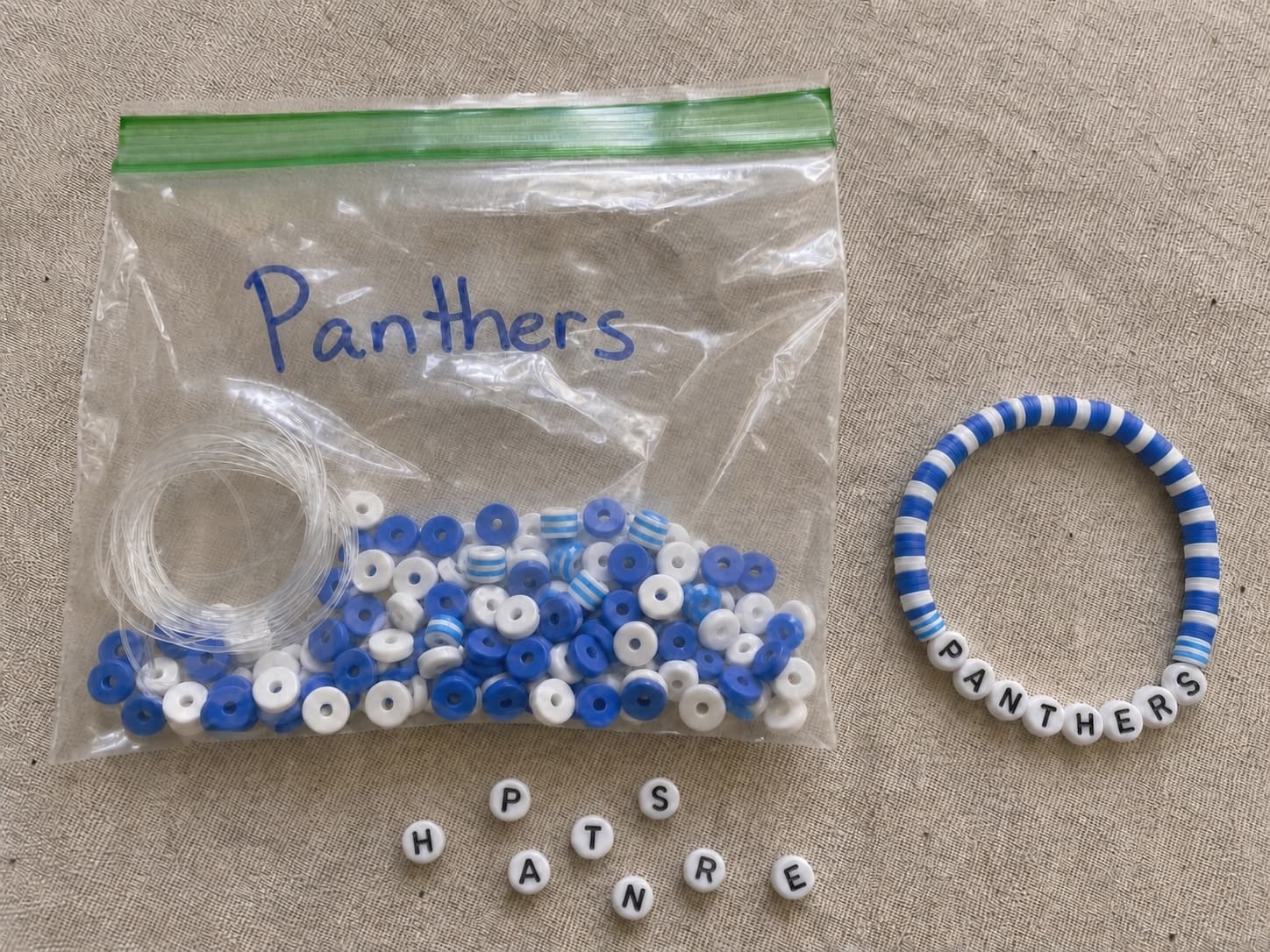 Handmade royal blue and white PANTHERS bracelet beside its clear DIY bead kit and loose letter beads