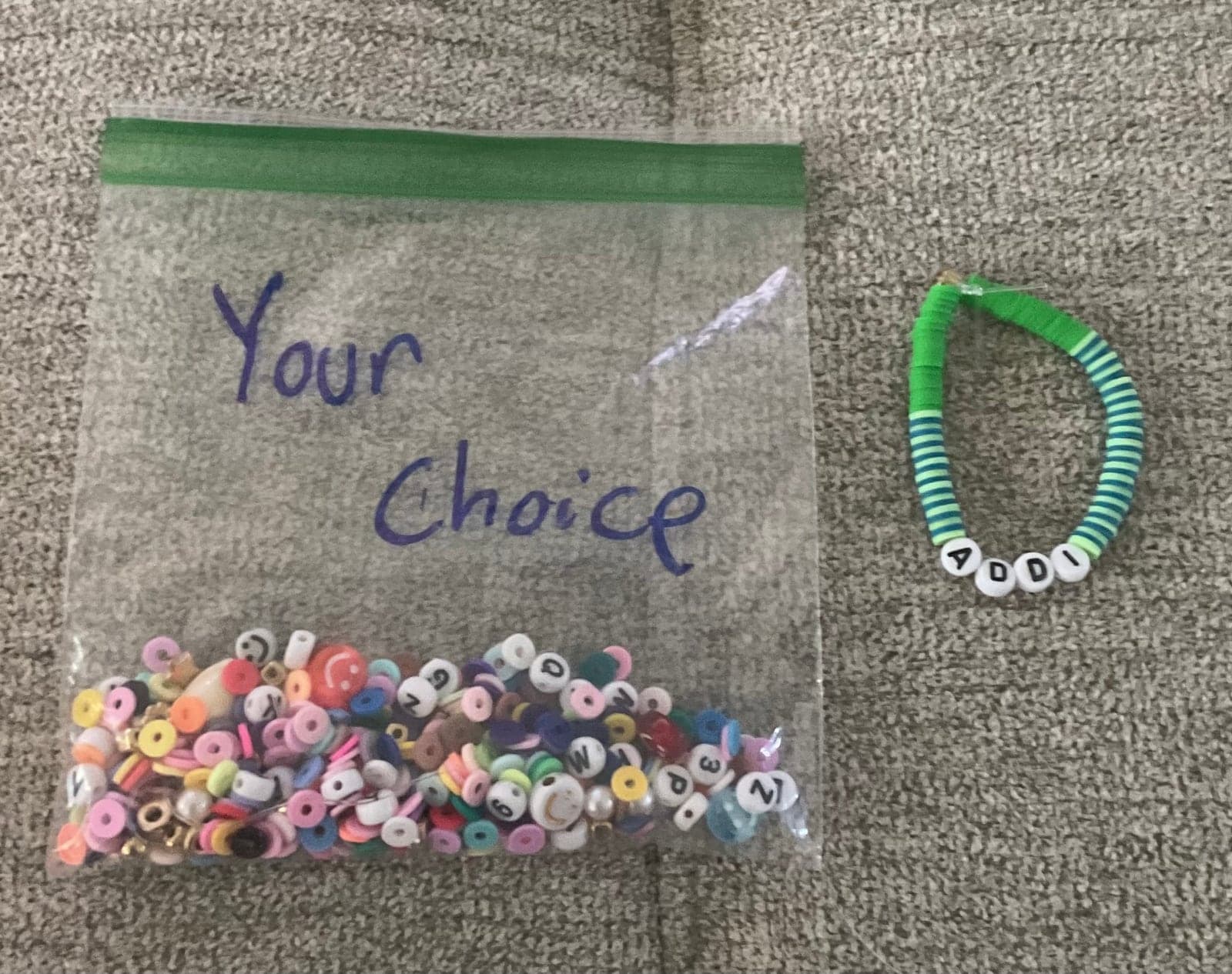 Colorful loose beads beside a handmade green and blue name bracelet